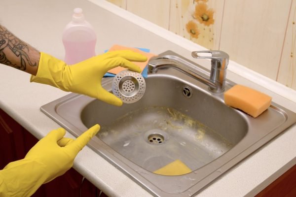 Cleaner in rubber gloves shows clean plughole protector of a kitchen sink